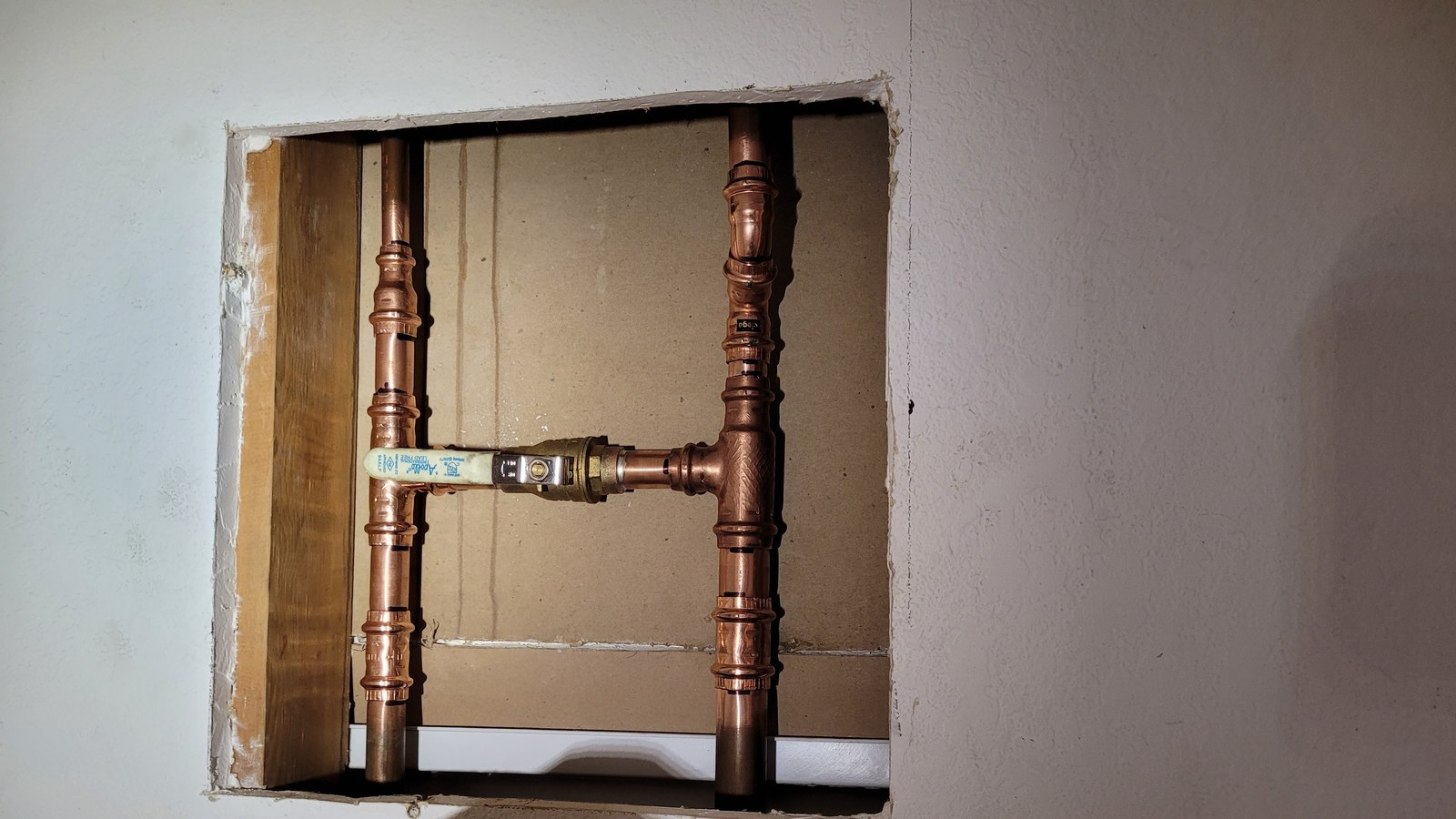 New ball valve with a yellow handle recessed between two copper risers inside a square wall opening