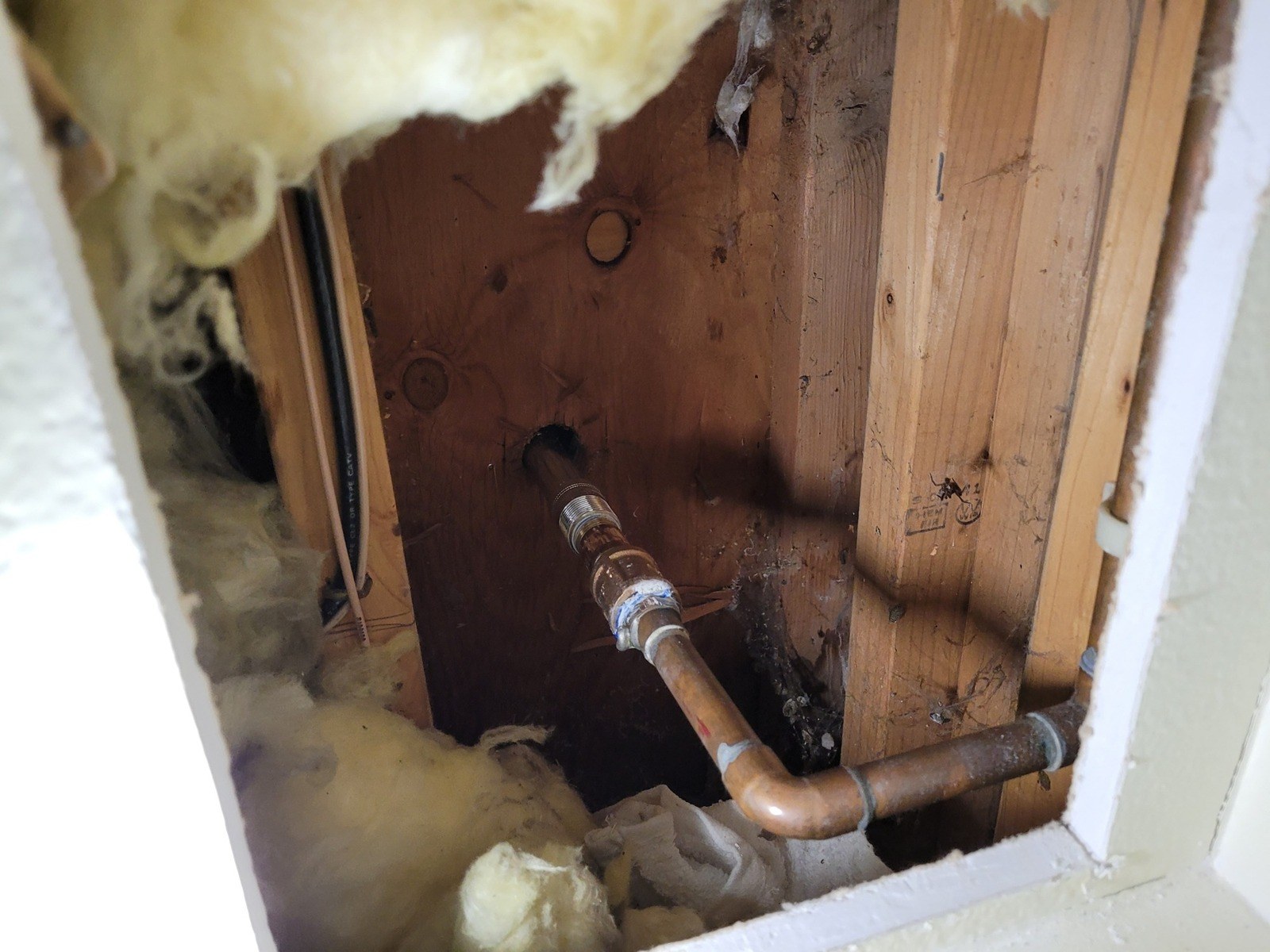 Opened basement drywall showing a new copper water line clamped to the framing and running through the rim joist to a replaced outdoor hose bib