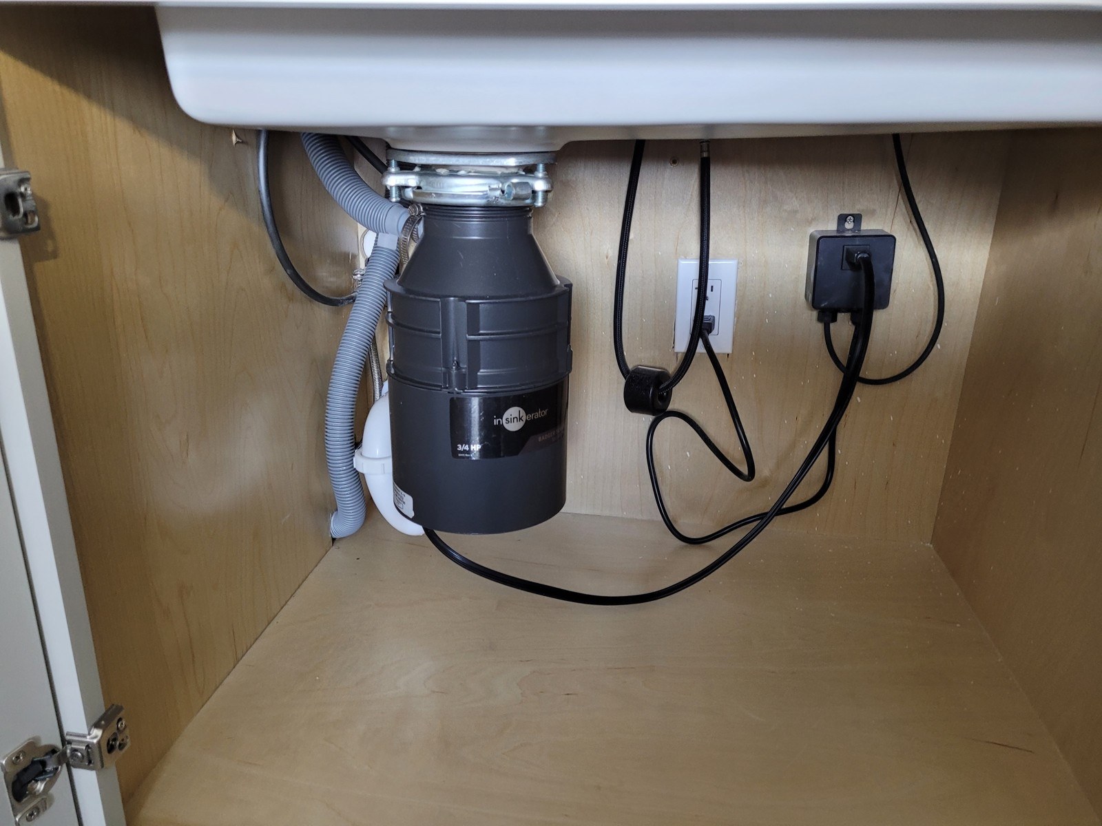 Under-sink cabinet in a condo kitchen with a black garbage disposal, a grey dishwasher drain hose and white PVC trap, the cabinet floor clean and dry