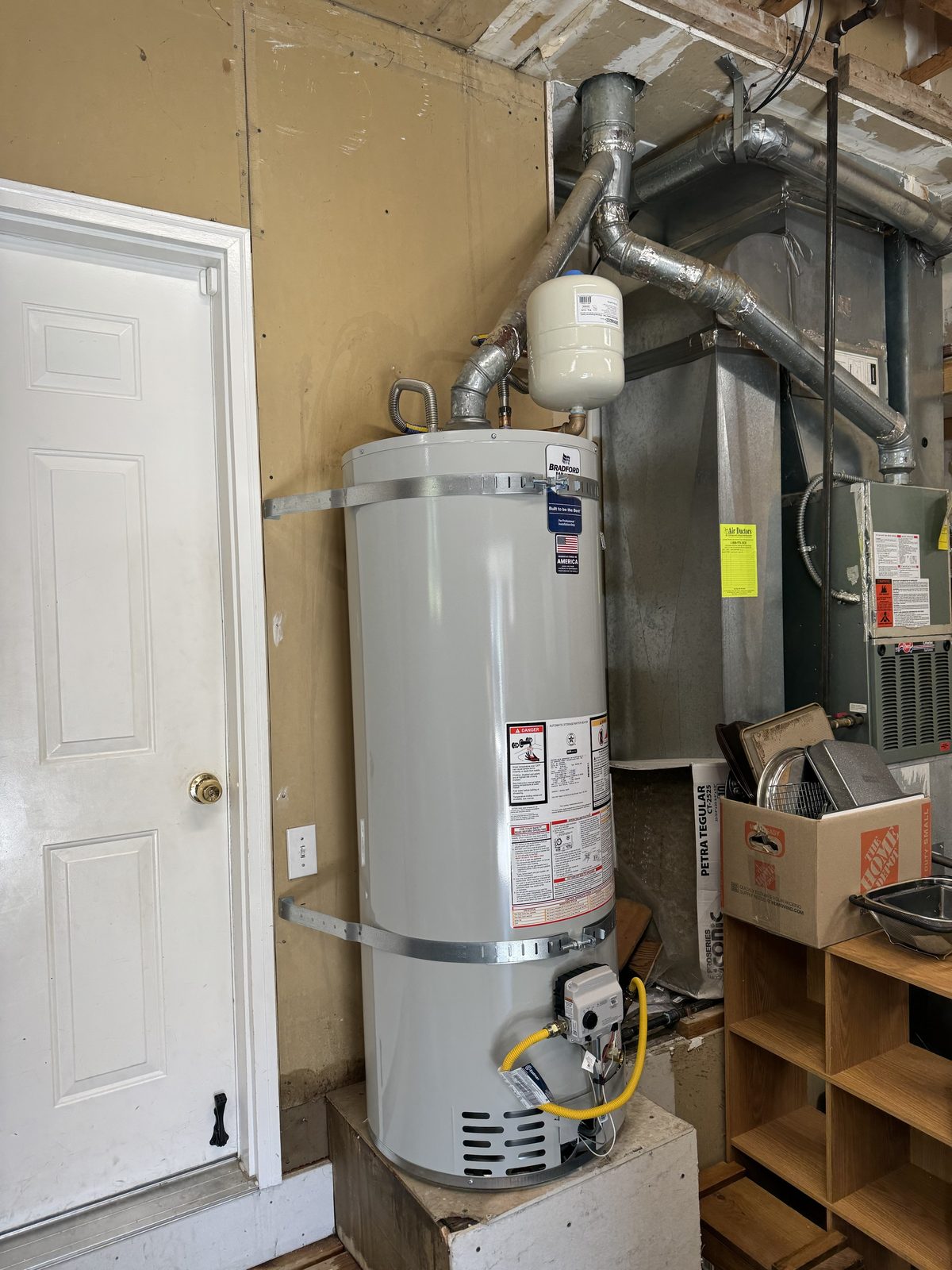 Gas tank water heater installed on a raised platform with seismic strapping and a thermal expansion tank